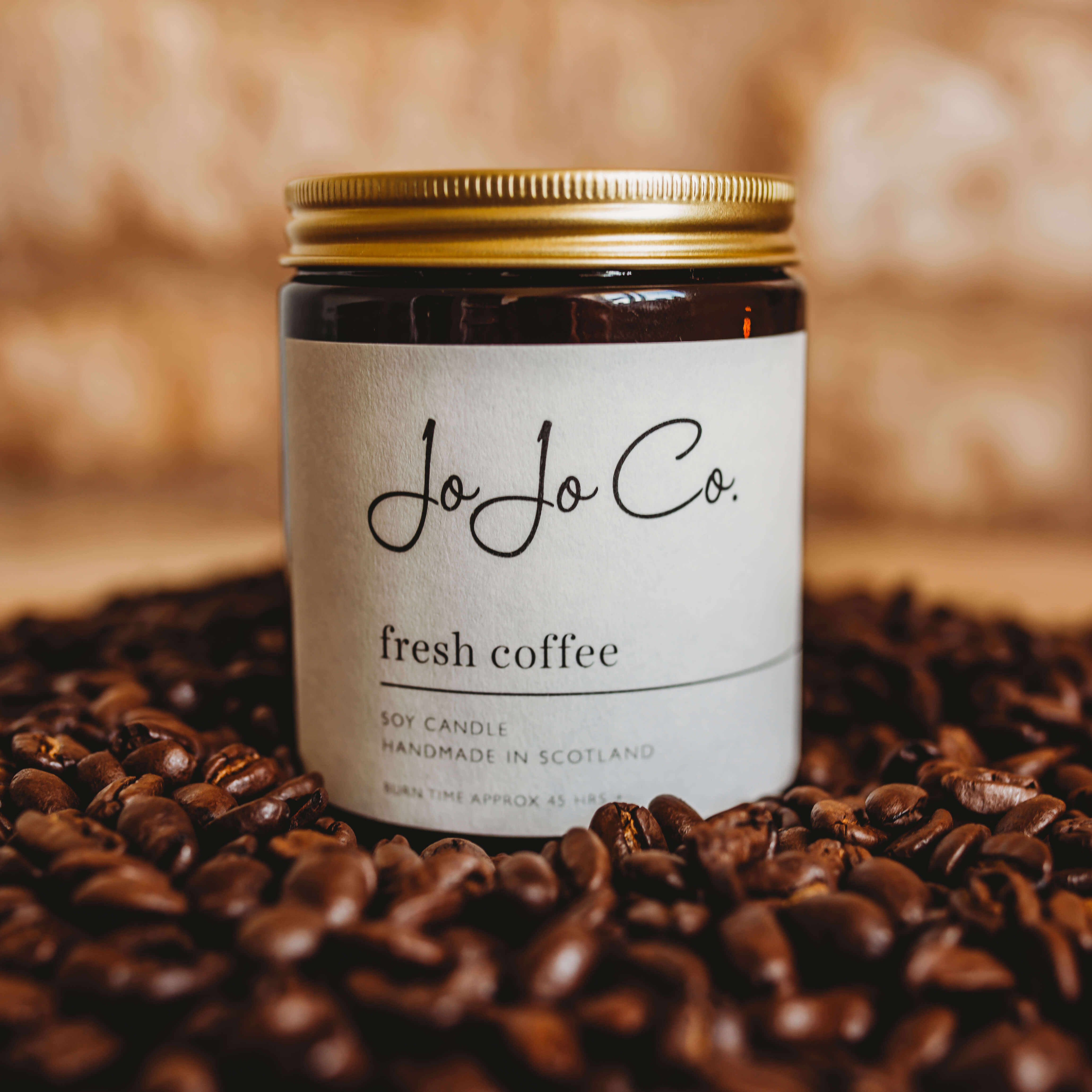 An amber jar with white label with 'fresh coffee' and the JoJo Co. logo. The jar has a glass lid and sits on top of coffee beans.
