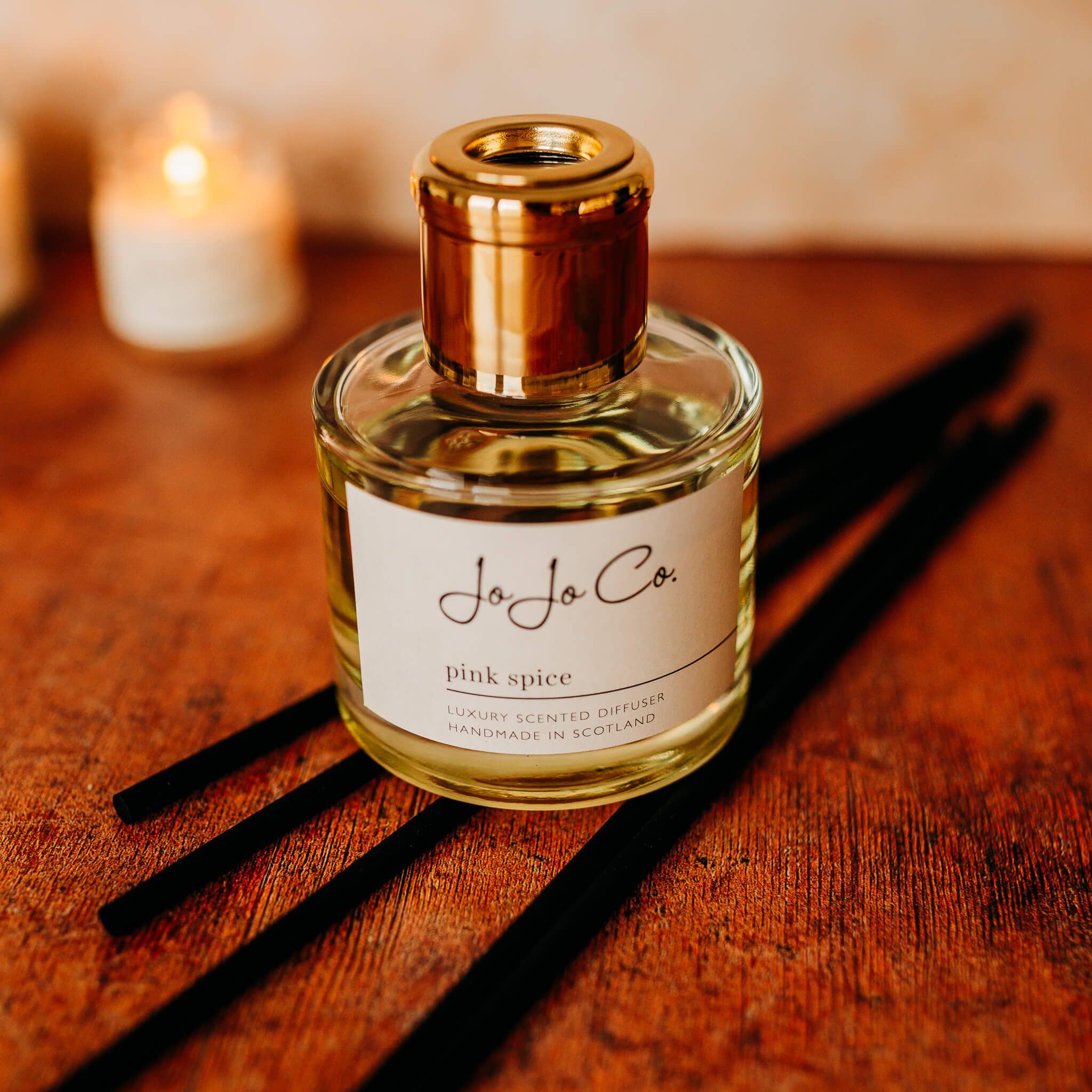 A glass jar diffuser and cardboard gift box with a white JoJo Co. label and gold lid.