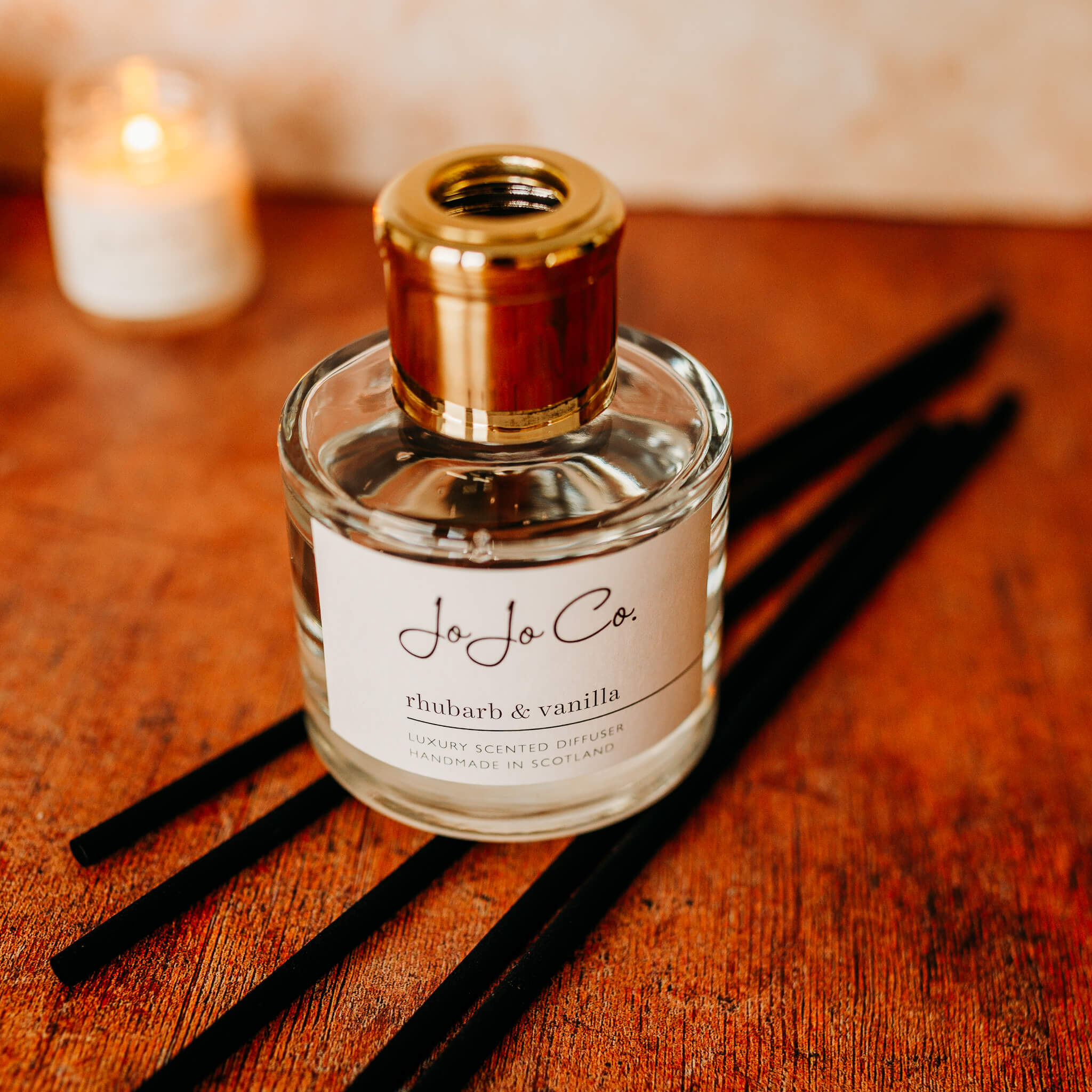A glass jar diffuser and cardboard gift box with a white JoJo Co. label and gold lid.