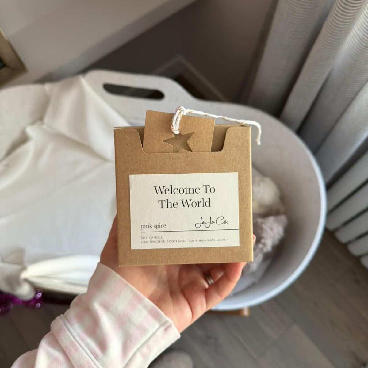 Hand holding a 'Welcome to the World' baby shower gift tag with a neutral background.
