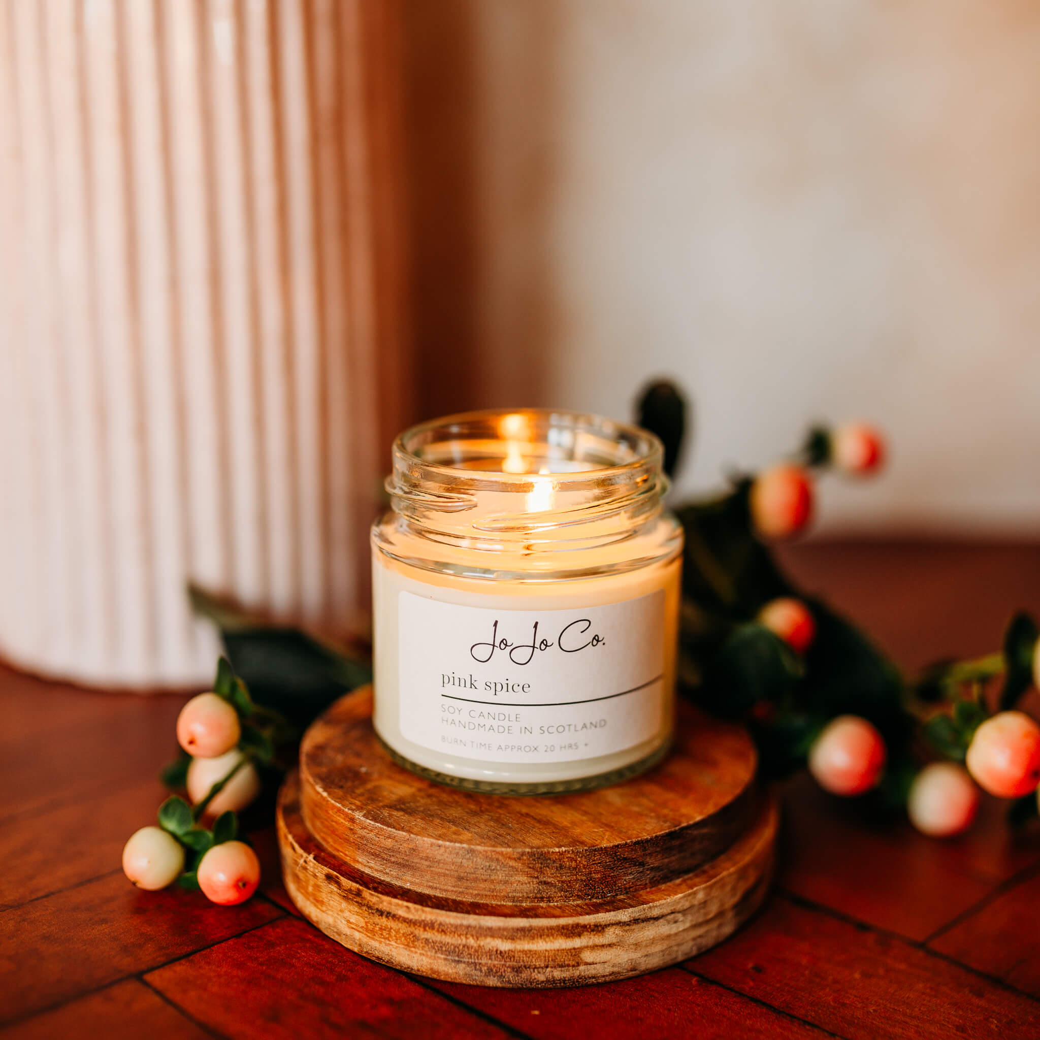 Lit Pink Spice candle on an oak candle base