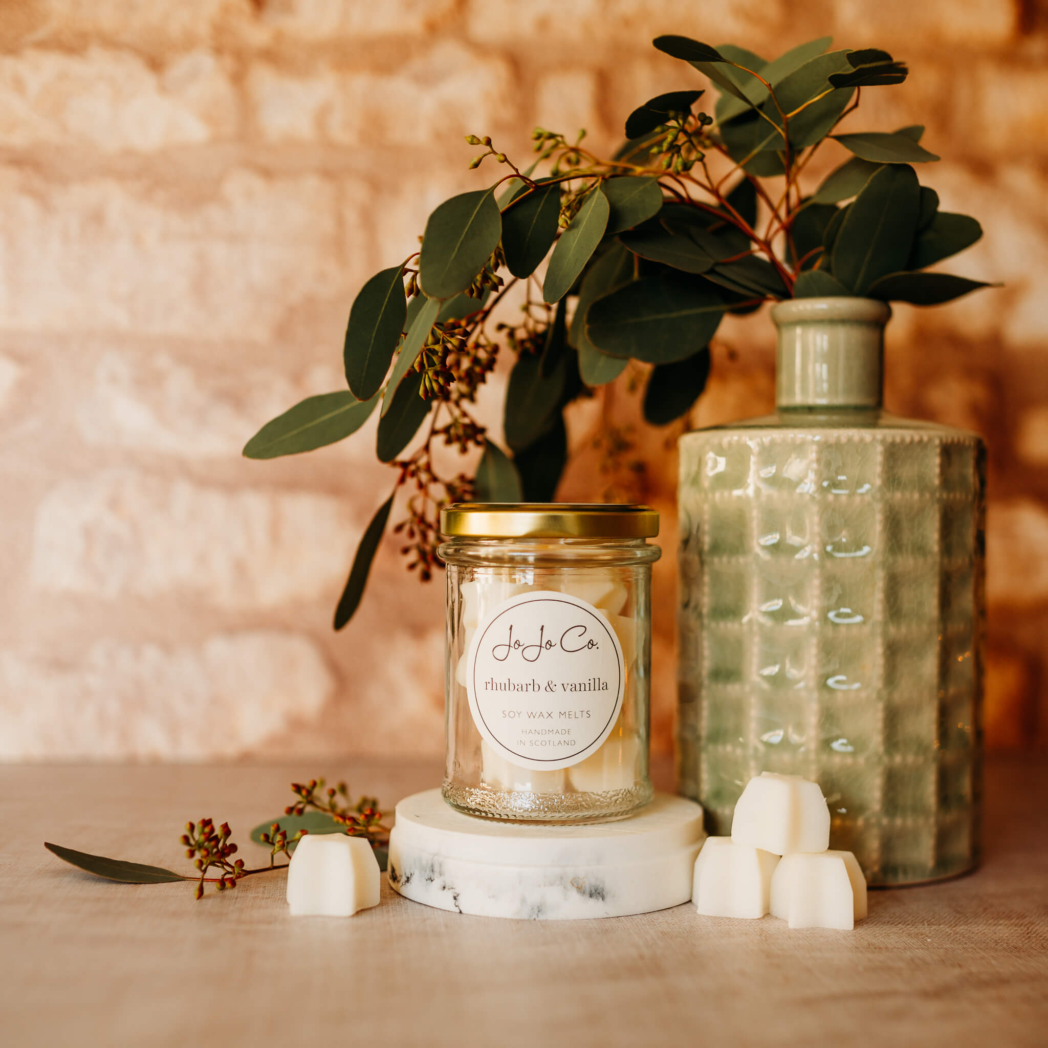 A glass jar filled with star shaped wax melts sits in a scene beside a green vase and piles of wax melts