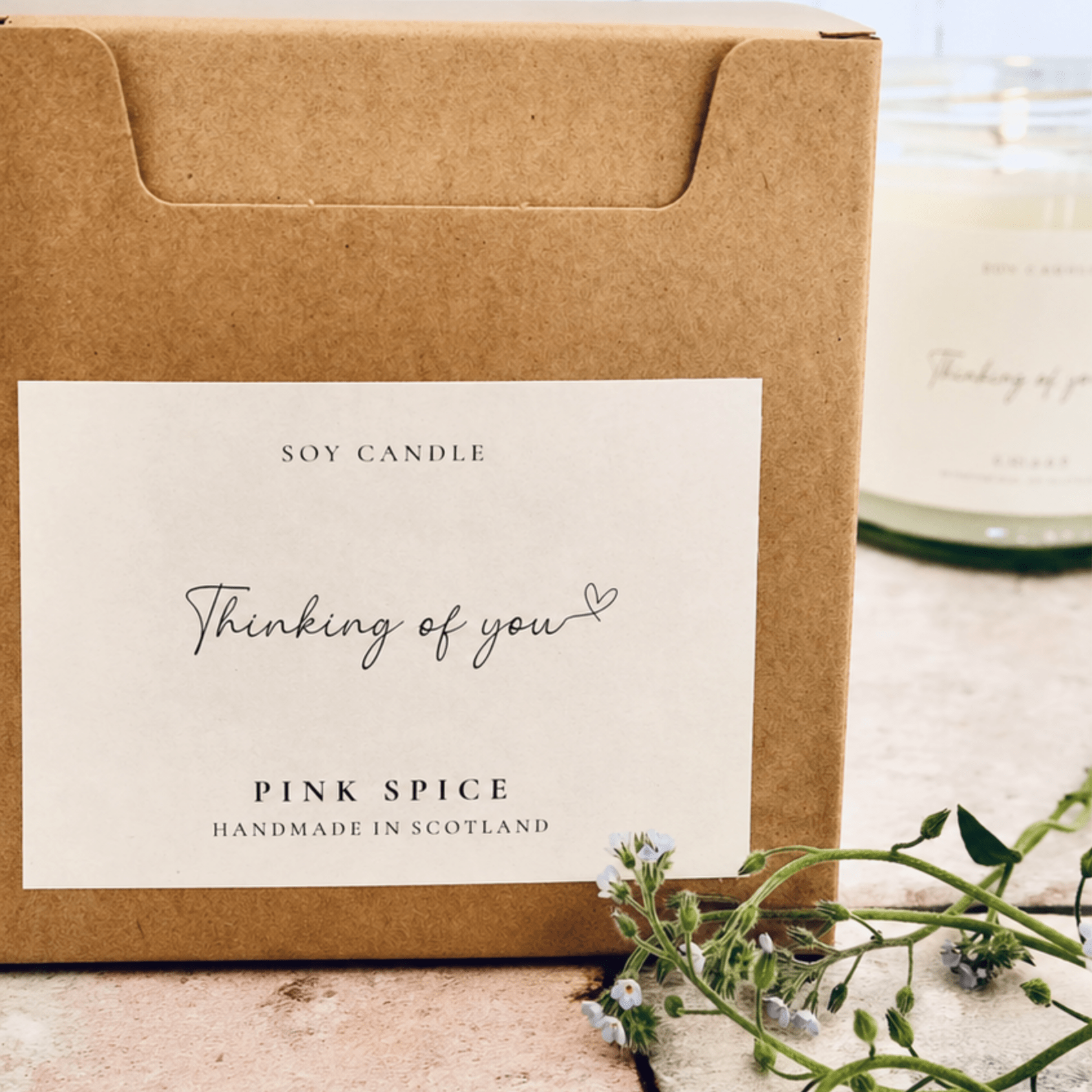 Soy candle packaging with 'Thinking of you' and 'Pink Spice' text on a wooden surface.
