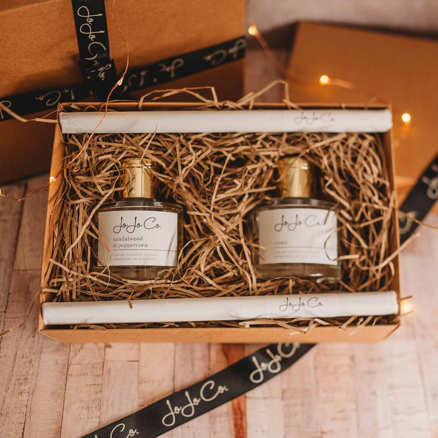 A glass jar diffuser and cardboard gift box with a white JoJo Co. label and gold lid.