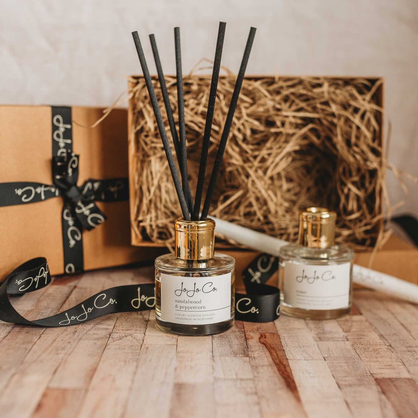 A glass jar diffuser and cardboard gift box with a white JoJo Co. label and gold lid.