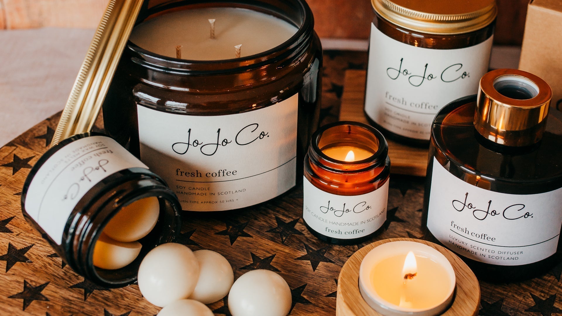 A luxury fresh coffee candle and diffuser set glowing warmly in a cosy home setting with rich amber glass and soft lighting 