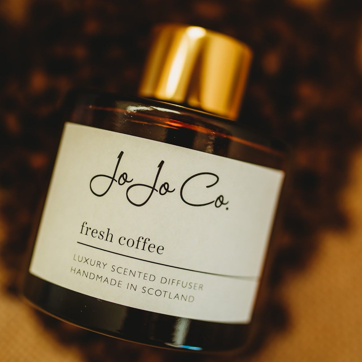 A close up of An amber glass jar diffuser with a white JoJo Co. label and gold lid. The label reads JoJo Co. Fresh Coffee