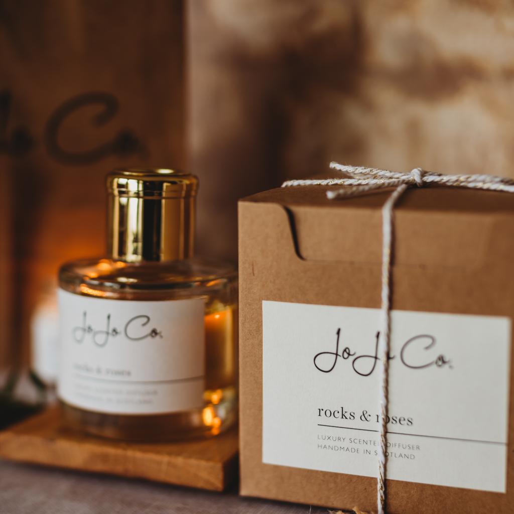 A glass jar diffuser and cardboard gift box with a white JoJo Co. label and gold lid.  