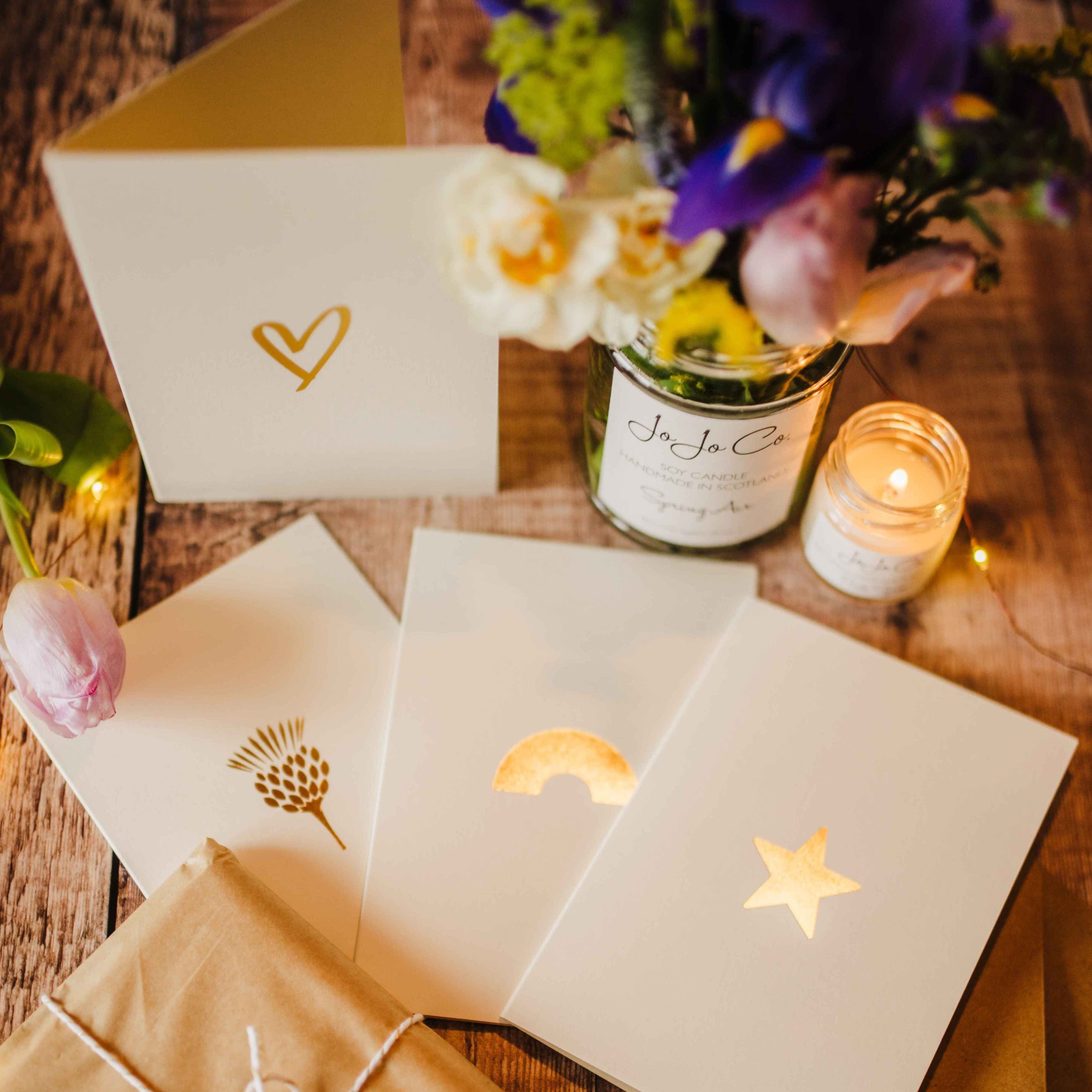 Selection of cream cards with gold motifs and a reused candle jar of Spring Air with flowers