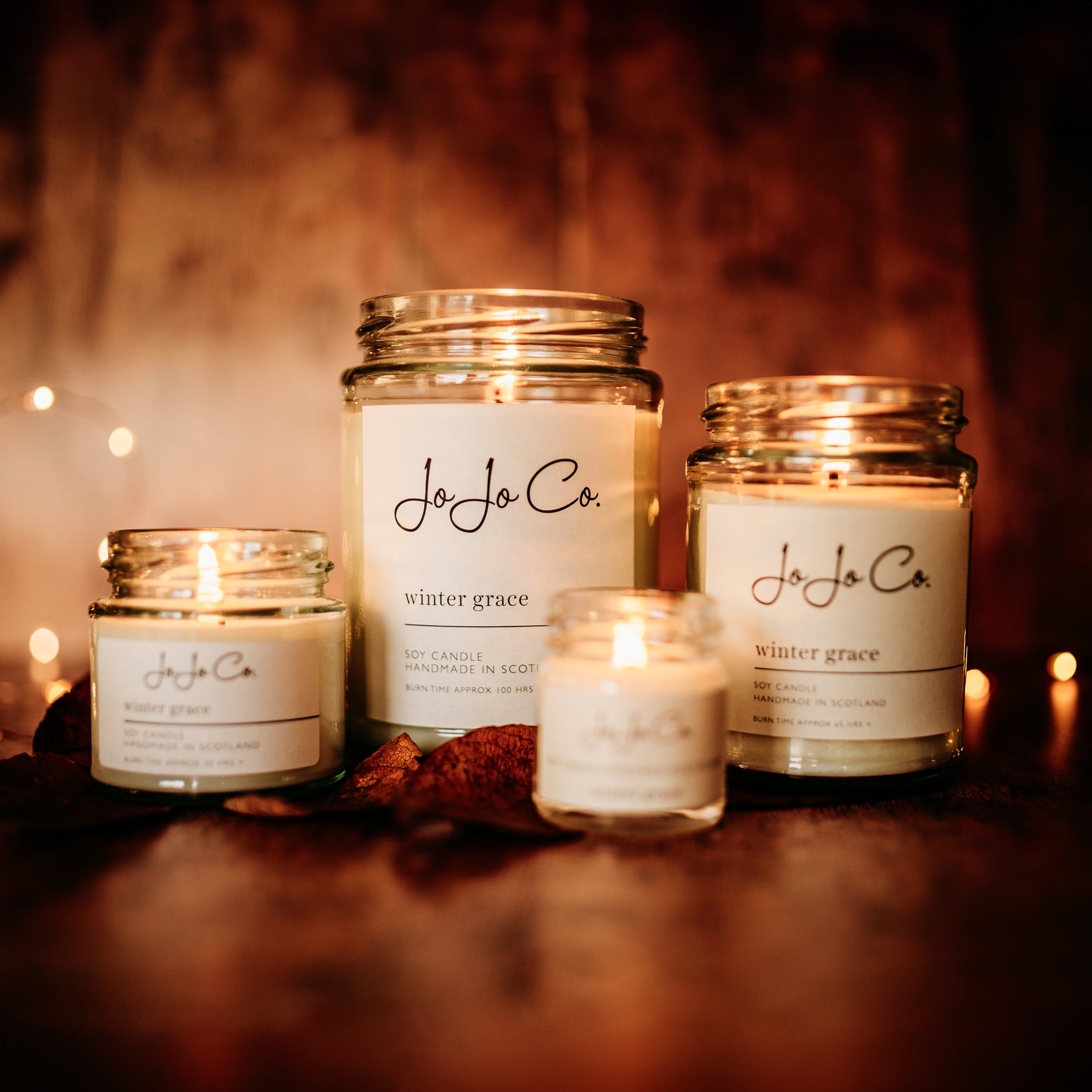 A selection of Winter Grace JoJo Co. candles. With dark background and sparkling fairy lights, the light from the candles casts a warm glow. 