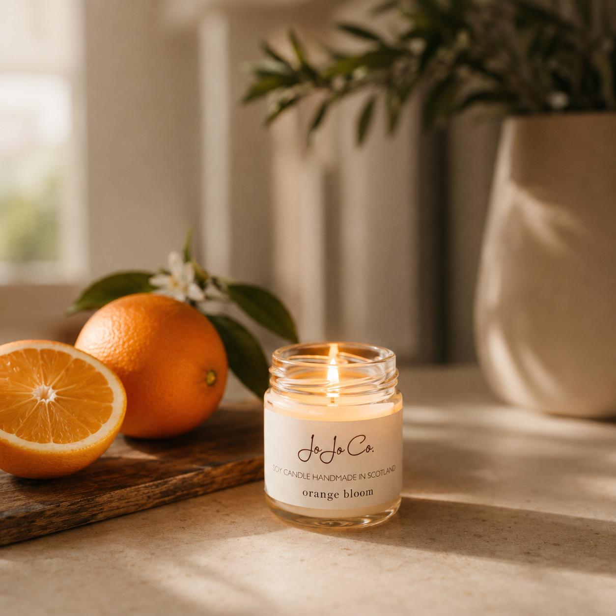Orange Bloom mini candle with oranges and a plant in the background